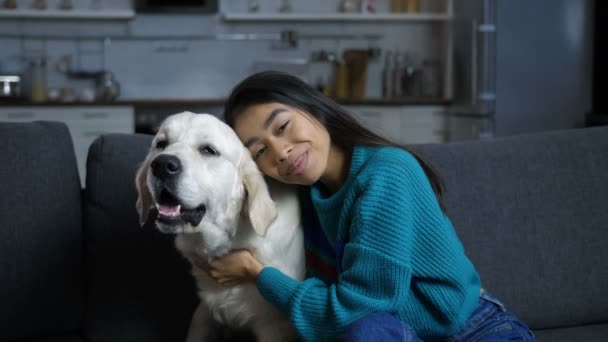 Joven mujer hindú acariciando y abrazando perro en sofá — Vídeo de stock