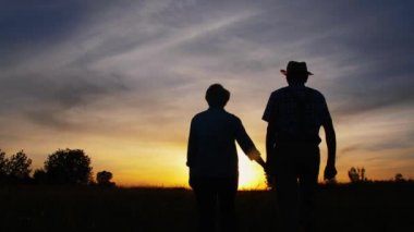 Gün batımında çayırda yürüyen öpüşen erkek ve kadın