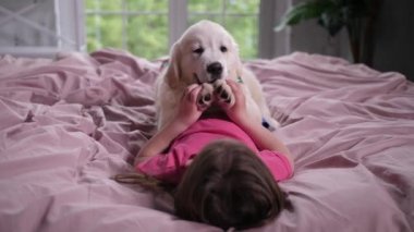 Küçük kız yatakta yatan köpek yavrusu evcil hayvan ile oynuyor