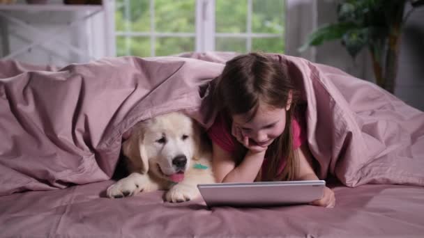Маленькая девочка смотрит мультик с щенком в постели — стоковое видео
