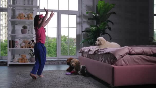 Menina bonito dançando para filhote de cachorro deitado na cama — Vídeo de Stock