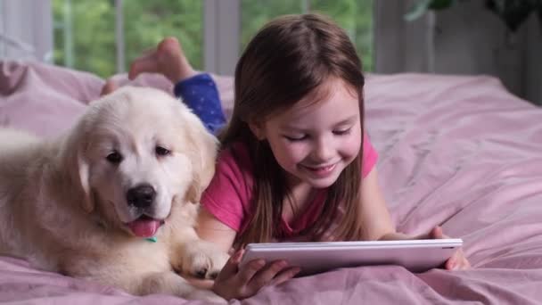 Sorrindo menina assistindo desenhos animados no tablet com filhote de cachorro — Vídeo de Stock