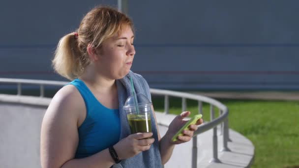 Regordeta mujer usando teléfono y bebiendo smoothie — Vídeos de Stock