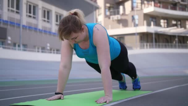 Mujer con sobrepeso haciendo flexiones en el estadio deportivo — Vídeos de Stock