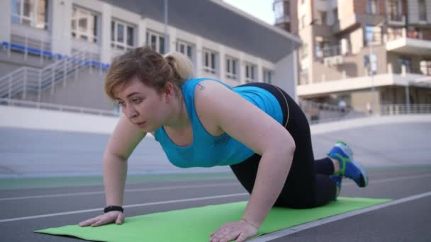 Plus-Size-Weibchen machen Liegestütze auf Sportplatz — Stockvideo