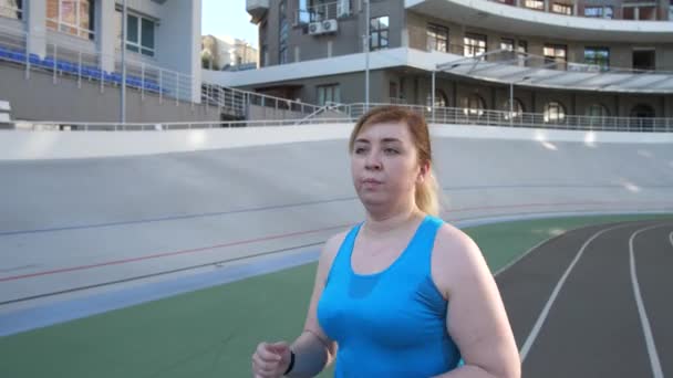 Femme active de plus de taille courant le long de la piste de stade — Video