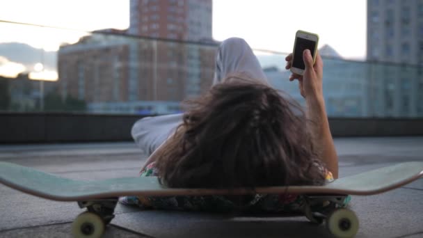 Skater surfeando en el teléfono acostado con la cabeza a bordo — Vídeo de stock