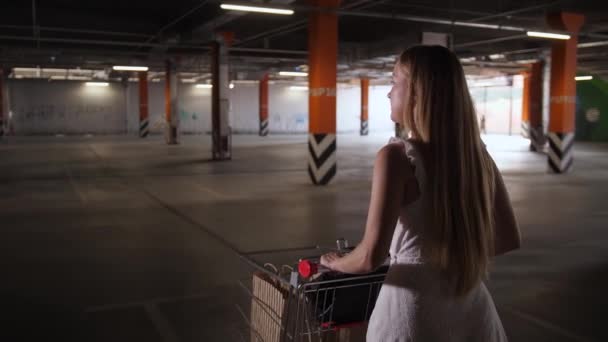 Frau läuft mit Einkaufswagen durch Parkplatz — Stockvideo
