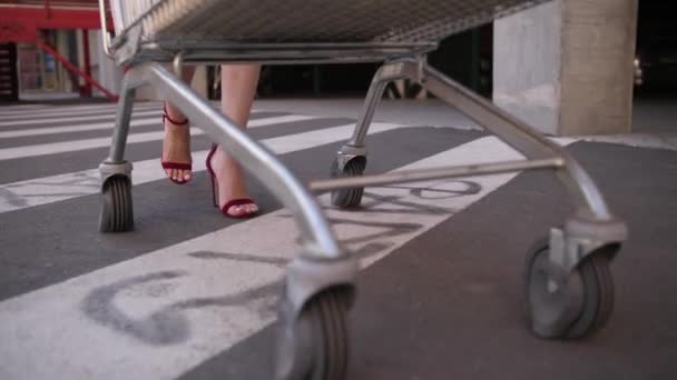 Pernas finas de mulher transportando carrinho de compras para carro — Vídeo de Stock