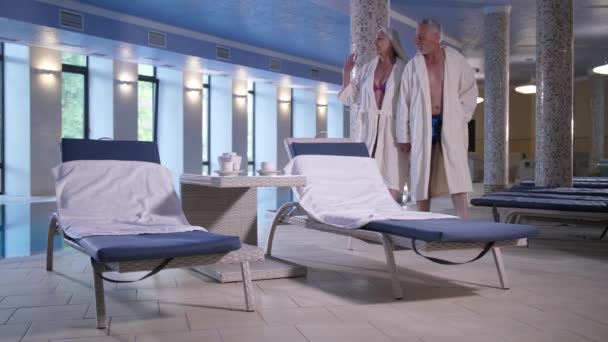 Elderly couple relaxing in hotel near pool indoors — Stock Video