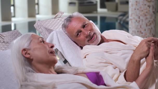 Elderly couple holding hands relaxing on sunbeds — Stock Video