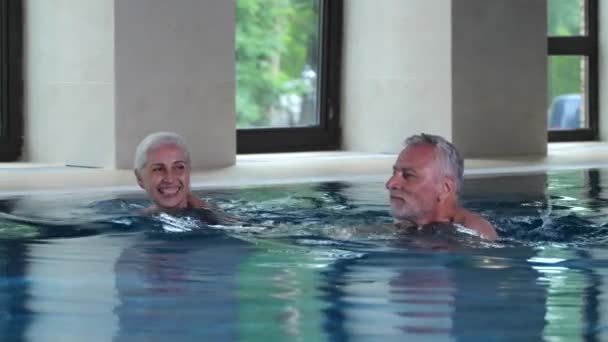 Feliz casal idoso nadando na piscina interior do hotel — Vídeo de Stock