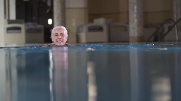 Mulher idosa atraente nadando na piscina do hotel — Vídeo de Stock