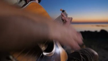 Geceleri kamp ateşi yakınında gitar çalan erkek eller