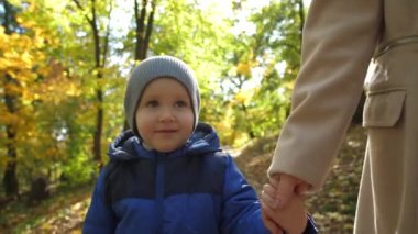 Annesiyle parkta yürüyen küçük bir çocuğun portresi.