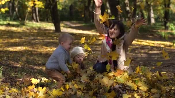 Счастливая мать с детьми бросает листья в парке — стоковое видео