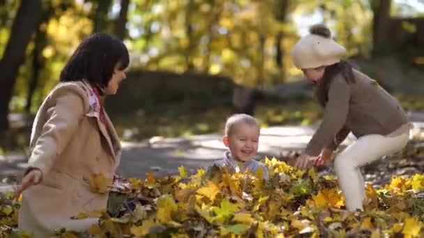 Счастливая мама с особенной девушкой бросает листья на мальчика — стоковое видео