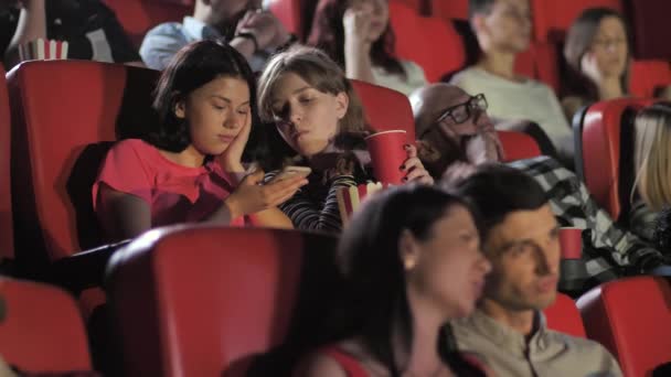 Meninas adolescentes usando smartphone durante o filme no cinema — Vídeo de Stock