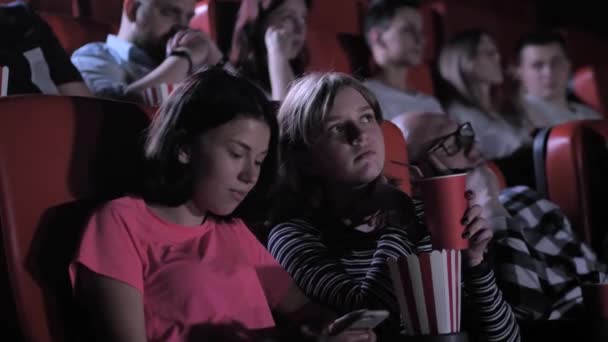 Due ragazze che usano il telefono durante film noioso nel cinema — Video Stock