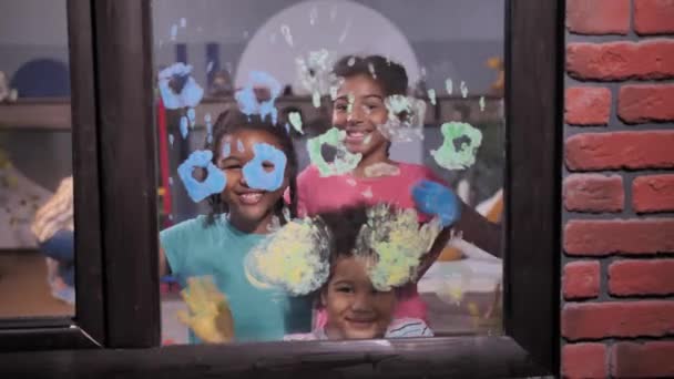 Niños sonrientes agitando palmas pintadas en la ventana — Vídeos de Stock