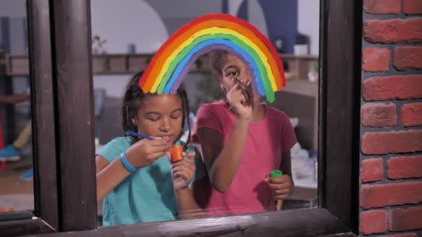 Vrolijke meisjes schilderen heldere regenboog op venster — Stockvideo