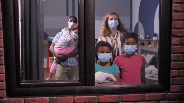 Familia diversa en máscaras faciales mirando por la ventana — Vídeos de Stock
