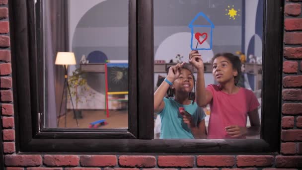 Felice misto razza sorelle pittura sul vetro della finestra — Video Stock