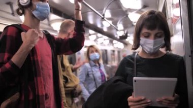 Metroda tablet kullanan maskeli genç bir kadın.