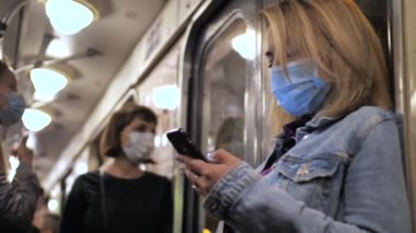 Metroda cep telefonu kullanan maskeli bir kadın.