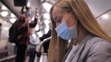 Güzel sarışın maskeli kadın metro treninde oturuyor.