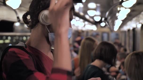 Młody mężczyzna w słuchawkach i masce twarzy w samochodzie metra — Wideo stockowe