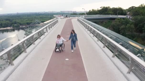 Plano aéreo de chica caminando con mamá en silla de ruedas — Vídeos de Stock