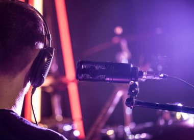 Kulaklık ve bir kayıt stüdyosu Studio mikrofon yakın ya da arka plan üzerinde odak modunda bir davul ile konser salonu olan kişi. Güzel arka plan bulanık renkli fenerler