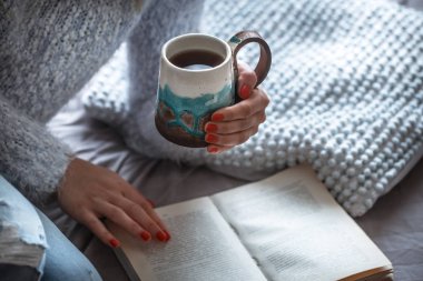 Kız güzel bir fincan çay onun elinde tutan ve okur bir kitap, sıcak içecekler ve okuma kavramı