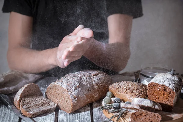 baker with flour in his hand and fresh bread on a beautiful wooden background, the concept of healthy food and bakery industry