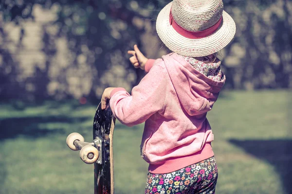 Liten Flicka Håller Skateboard Och Spelar Utanför Mot Bakgrund Grön — Stockfoto