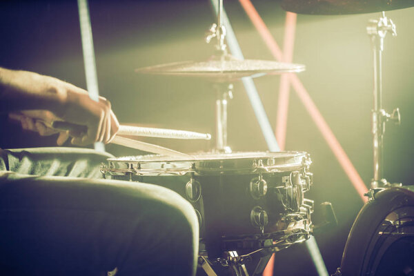 the man plays the drums, the game is on the working drum with sticks close-up. On the background of colored lights. Musical concept with a working drum.