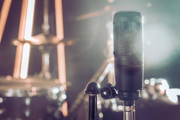 The microphone in a recording Studio or a concert hall close up of drum kit and an acoustic guitar in the background. Beautiful blurred background of colored lanterns. Musical concept in vintage style