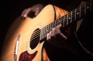 Adam koyu arka plan üzerinde gitar closeup akustik gitar çalmak. Müzikal bir kavram.