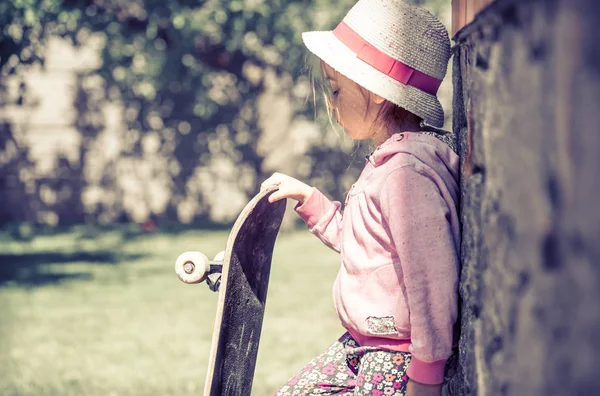 Uma menina na moda está segurando um skate e brincando fora, as belas emoções de uma criança . — Fotografia de Stock
