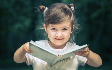 küçük şirin küçük kız parkta yeşil doğanın bir arka plan üzerine bir kitap okuyor