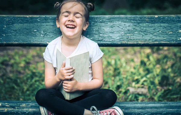 Kleines Nettes Mädchen Sitzt Auf Einer Bank Und Liest Ein — Stockfoto