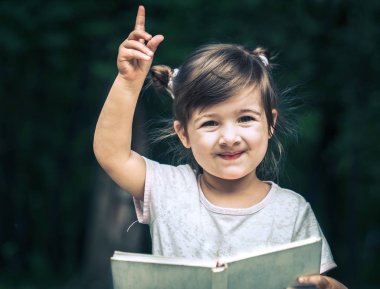 küçük şirin küçük kız parkta yeşil doğanın bir arka plan üzerine bir kitap okuyor