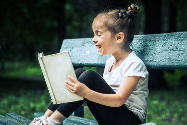 küçük sevimli kız bir bankta oturan ve parkta yeşil doğanın bir arka plan üzerine bir kitap okuma