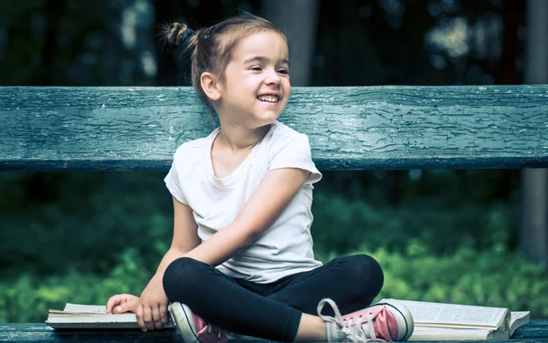 Kleines Nettes Mädchen Sitzt Auf Einer Bank Und Liest Ein — Stockfoto