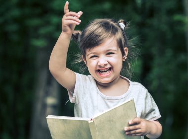 küçük şirin küçük kız parkta yeşil doğanın bir arka plan üzerine bir kitap okuyor
