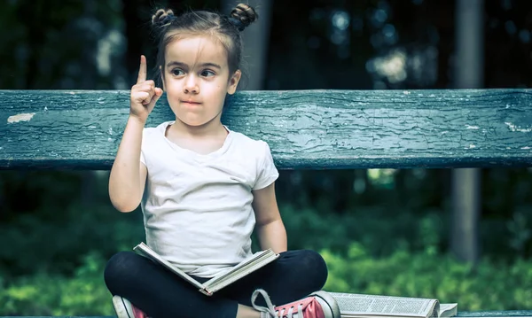 Kleines Nettes Mädchen Sitzt Auf Einer Bank Und Liest Ein — Stockfoto
