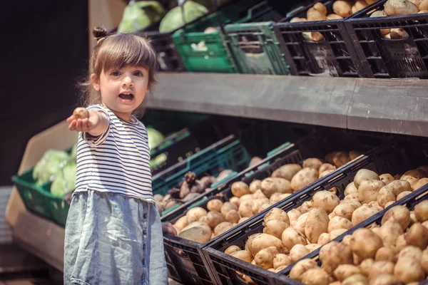 little girl with a potato in hands near the counter in the store, the concept of shopping for food
