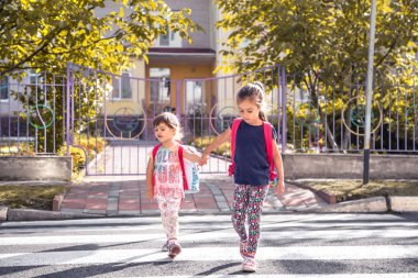 Çocukların okula, mutlu öğrenciler okul sırt çantaları ile gitmek ve birlikte, el ele tutuşarak, eğitimle kızlar, metin için yer kavramını karşıdan karşıya