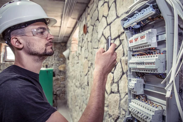 a male electrician works in a switchboard with an electrical connecting cable, connects the equipment with tools, the concept of complex work, space for text